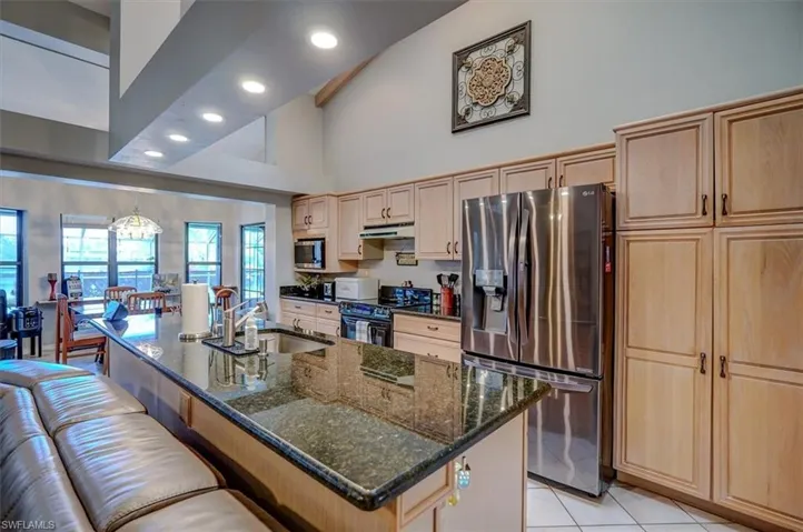 Kitchen featuring under cabinet range hood, a sink, appliances with stainless steel finishes, an island with sink, and dark stone countertops