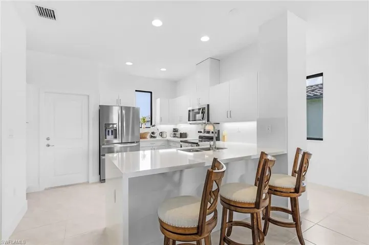 Kitchen with stainless steel appliances, white cabinetry, a peninsula, a breakfast bar area, and light stone countertops