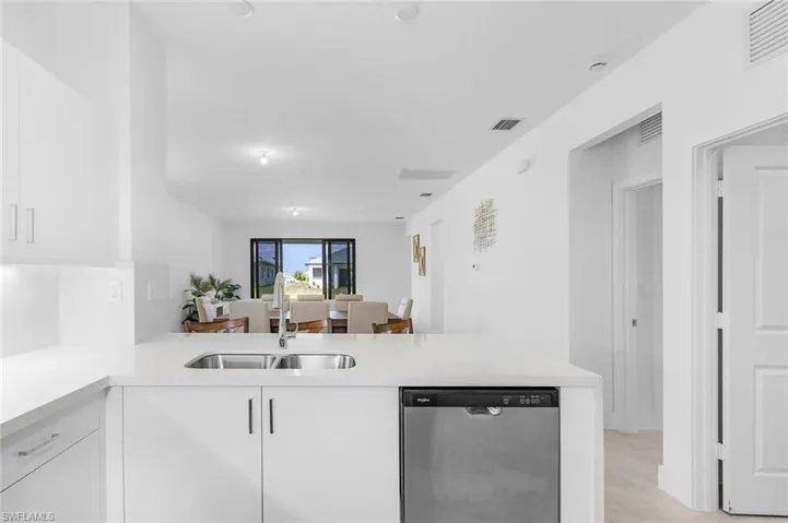 Kitchen with a peninsula, dishwasher, white cabinets, and light stone countertops