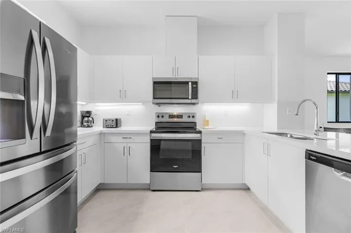 Kitchen with stainless steel appliances, light stone counters, white cabinetry, and a peninsula