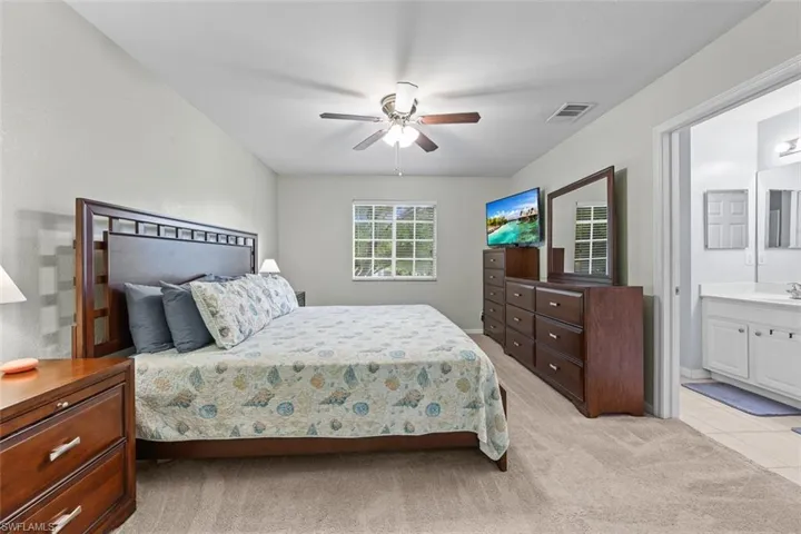Bedroom featuring light carpet, a ceiling fan, ensuite bathroom, and light tile patterned floors