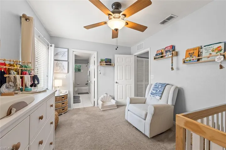 Bedroom featuring a crib, light carpet, ensuite bathroom, and ceiling fan