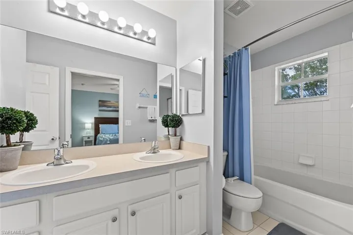 Bathroom featuring connected bathroom, light tile patterned flooring, shower / bath combination with curtain, and double vanity