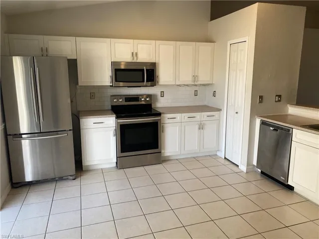 Kitchen featuring white cabinets, appliances with stainless steel finishes, backsplash, lofted ceiling, and light countertops