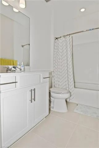 Bright bathroom featuring a white vanity with brushed nickel hardware, a sink with a chrome faucet, a large mirror, a bathtub with an overhead shower, and light-toned floor tiles