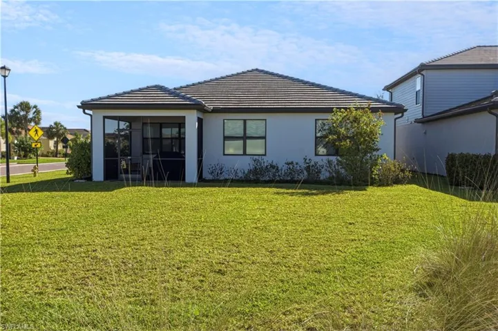 Rear exterior with a screened patio, tile roof, and a manicured lawn