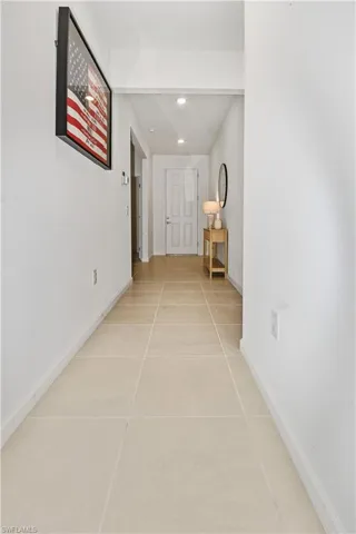 Long hallway with light-toned tiled flooring, white walls, and recessed lighting