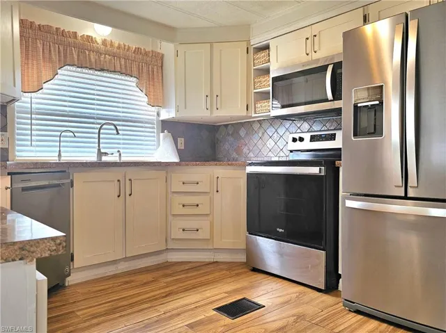 Kitchen with appliances with stainless steel finishes, backsplash, light wood-style floors, open shelves, and dark stone countertops