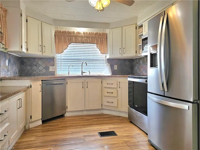 Kitchen with appliances with stainless steel finishes, light wood-style flooring, light stone countertops, and decorative backsplash
