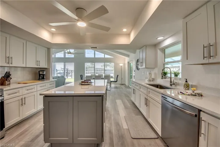 Kitchen featuring dishwasher, a raised ceiling, ceiling fan, a sink, and a center island