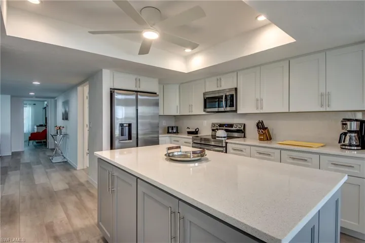 Kitchen featuring stainless steel appliances, a kitchen island, a ceiling fan, light wood-style flooring, and light stone countertops