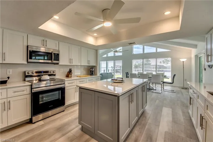 Kitchen with stainless steel appliances, a ceiling fan, a raised ceiling, light countertops, and recessed lighting