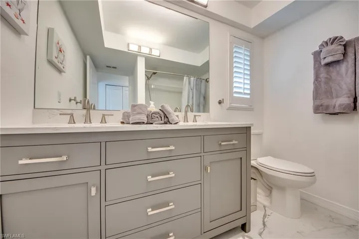 Full bathroom featuring double vanity, baseboards, marble look tiles, toilet, and a shower with shower curtain