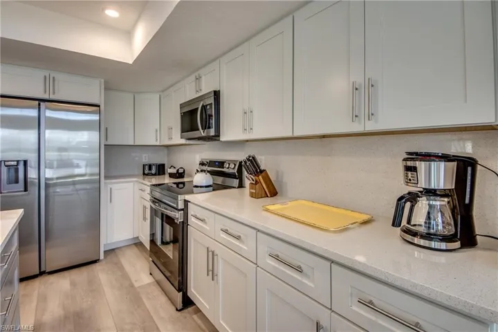Kitchen with stainless steel appliances, white cabinets, light wood-type flooring, light stone counters, and recessed lighting