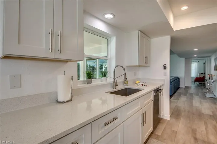 Kitchen featuring a sink, dishwasher, white cabinetry, light stone countertops, and recessed lighting