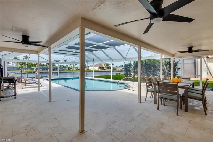 Outdoor pool featuring ceiling fan, a patio area, outdoor dining space, glass enclosure, and a water view