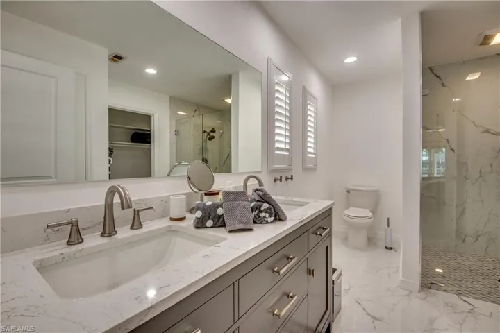 Full bath with a marble finish shower, double vanity, marble finish flooring, toilet, and a spacious closet