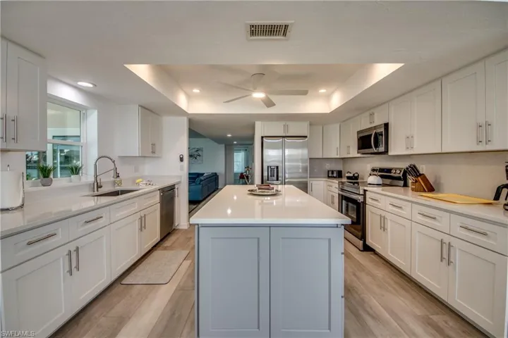 Kitchen featuring appliances with stainless steel finishes, a sink, a tray ceiling, white cabinetry, and recessed lighting