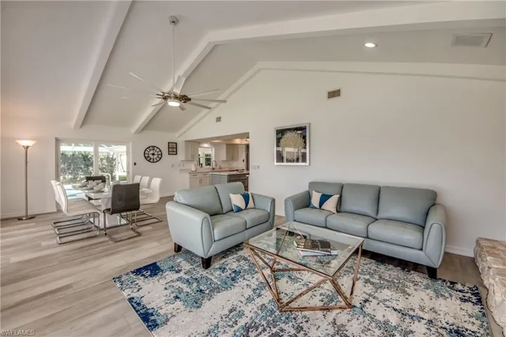 Living room featuring light wood-style flooring, ceiling fan, baseboards, beam ceiling, and high vaulted ceiling