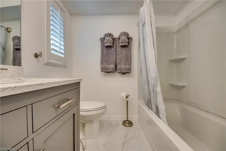 Bathroom featuring marble finish floors, toilet, vanity, baseboards, and shower / bathtub combination with curtain