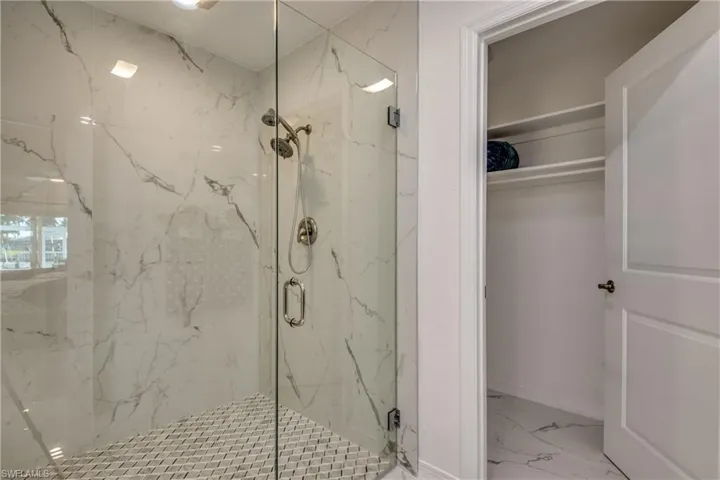 Bathroom with marble look tile flooring, a marble finish shower, and a walk in closet
