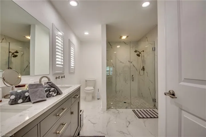 Full bath with a marble finish shower, marble finish flooring, recessed lighting, double vanity, and toilet