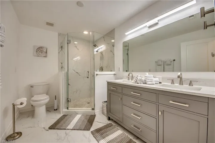 Bathroom featuring double vanity, marble look tile flooring, a marble finish shower, toilet, and baseboards