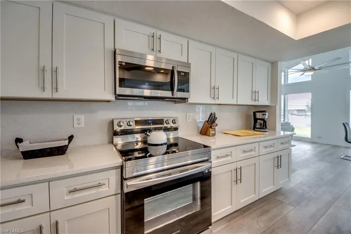 Kitchen with stainless steel appliances, white cabinetry, light wood finished floors, ceiling fan, and backsplash