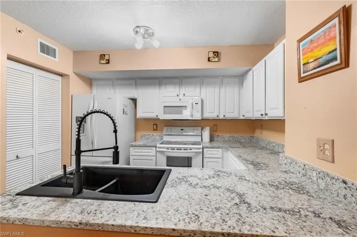 Kitchen with sink, white appliances, white cabinetry, light stone counters, and a textured ceiling