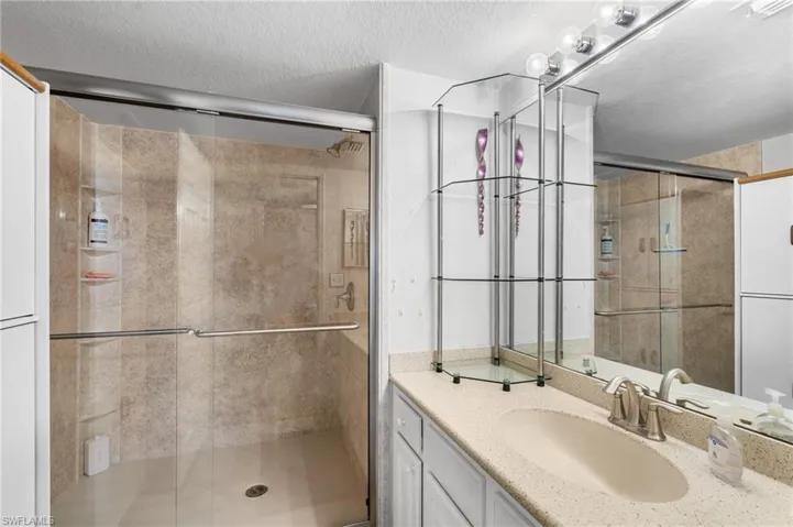 Bathroom with vanity, a shower with door, and a textured ceiling