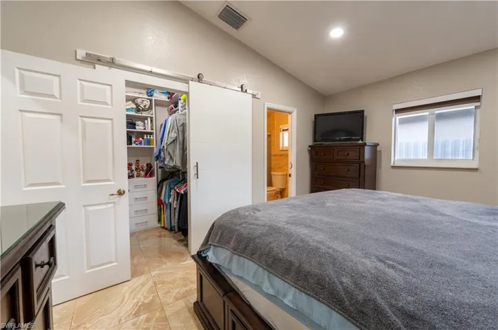 Bedroom featuring lofted ceiling, a walk in closet, a barn door, light marble finish floors, and connected bathroom