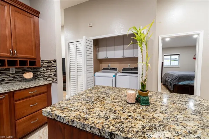Kitchen with separate washer and dryer, light stone countertops, brown cabinetry, and backsplash