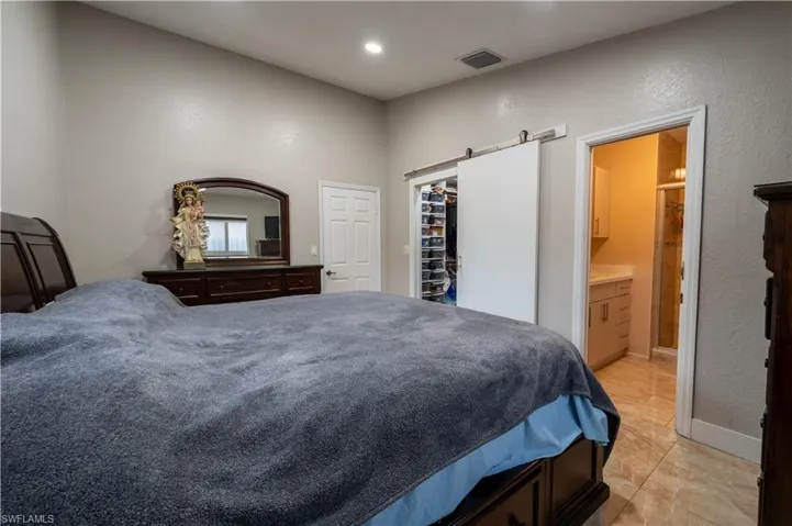 Bedroom featuring a barn door, connected bathroom, a textured wall, light marble finish floors, and a walk in closet