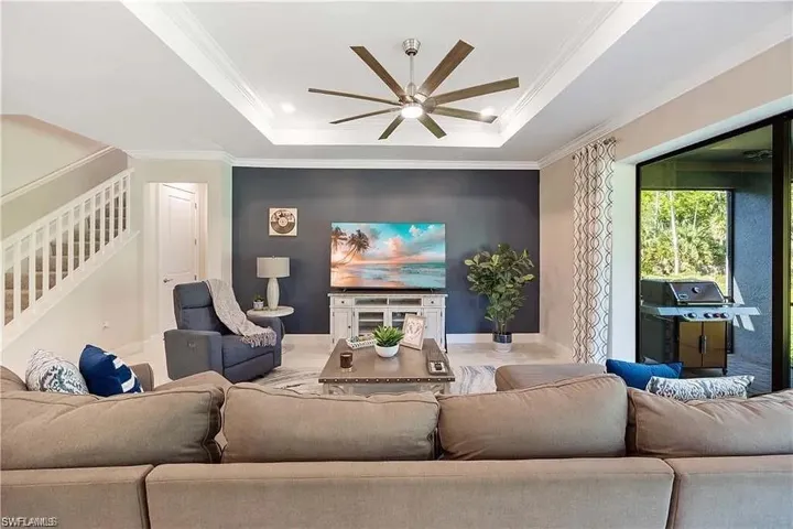 Living room featuring a ceiling fan, a raised ceiling, stairway, ornamental molding, and baseboards