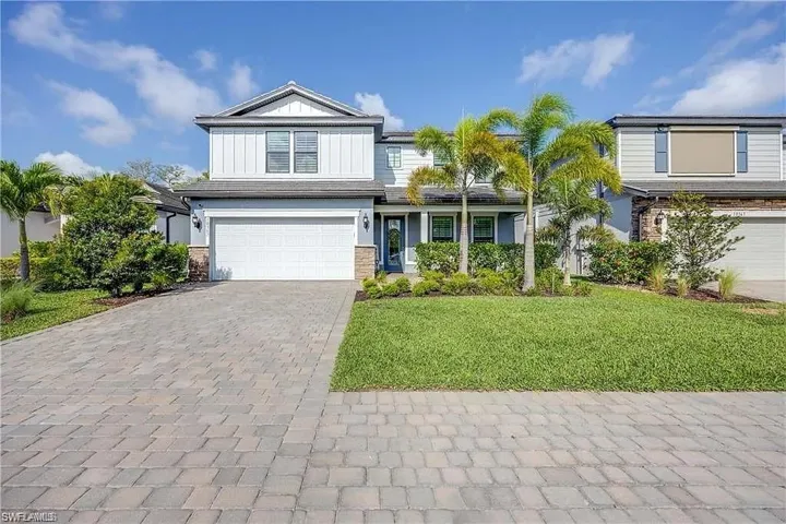 View of front of property with a garage, decorative driveway, a front lawn, stone siding, and board and batten siding