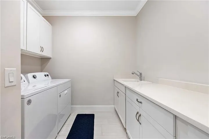 Washroom featuring washer and clothes dryer, cabinet space, crown molding, and baseboards