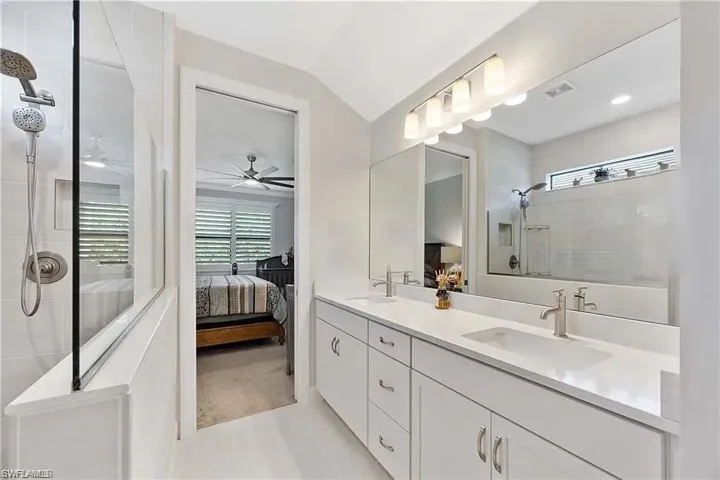 Ensuite bathroom with a tile shower, ceiling fan, double vanity, and vaulted ceiling