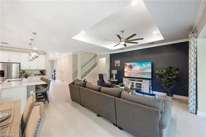 Living room with stairway, crown molding, a ceiling fan, a raised ceiling, and recessed lighting