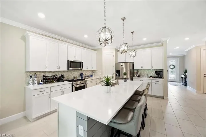 Kitchen featuring stainless steel appliances, an island with sink, decorative backsplash, crown molding, and light countertops