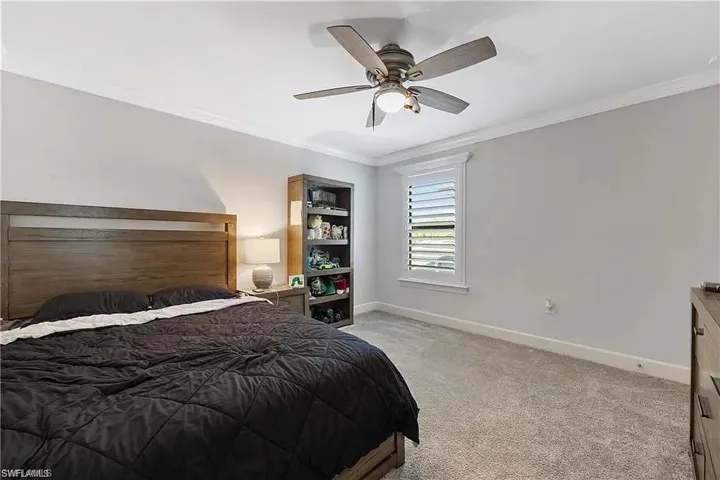 Bedroom with light colored carpet, crown molding, baseboards, and a ceiling fan