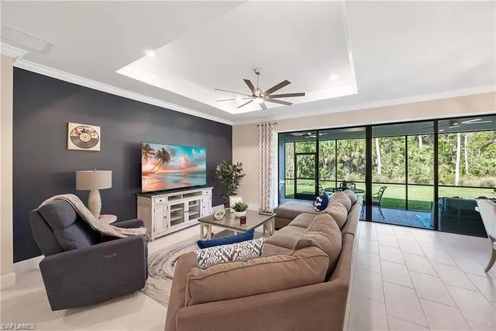 Living area featuring a ceiling fan, a raised ceiling, ornamental molding, light tile patterned floors, and baseboards