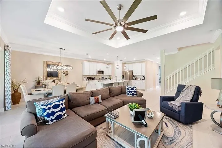 Living area with a tray ceiling, a ceiling fan, stairs, crown molding, and recessed lighting