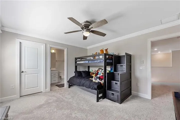 Carpeted bedroom featuring crown molding, baseboards, ensuite bath, and ceiling fan