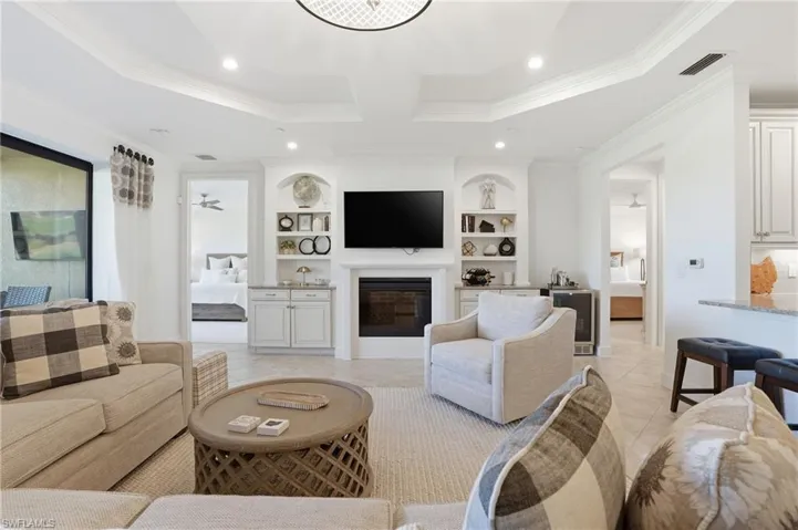 Living area featuring built in features, light tile patterned floors, a glass covered fireplace, recessed lighting, and crown molding
