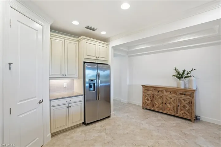 Kitchen with stainless steel refrigerator with ice dispenser, cream cabinets, light stone countertops, tasteful backsplash, and recessed lighting