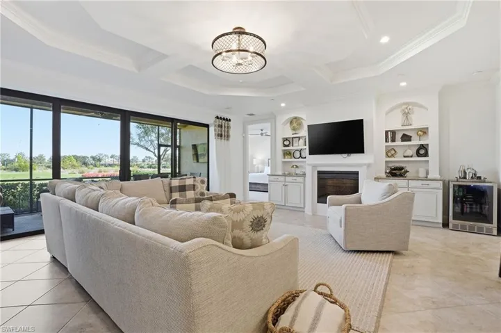 Living area with built in shelves, beverage cooler, a chandelier, light tile patterned flooring, and a glass covered fireplace
