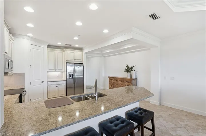 Kitchen with a peninsula, a breakfast bar area, stainless steel appliances, light stone counters, and ornamental molding