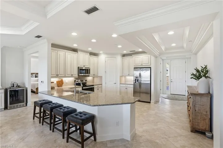 Kitchen featuring crown molding, dark stone countertops, appliances with stainless steel finishes, wine cooler, and a peninsula