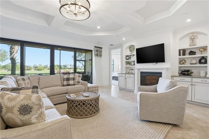 Living area with a glass covered fireplace, a chandelier, light tile patterned flooring, built in features, and coffered ceiling