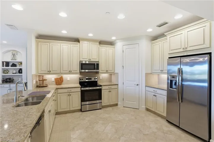 Kitchen featuring cream cabinetry, stainless steel appliances, light stone countertops, ornamental molding, and recessed lighting